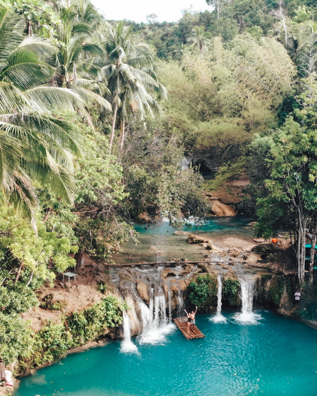 A drone shot of Cambugahay Falls in Siquijor, Philippines, with a couple standing on a raft