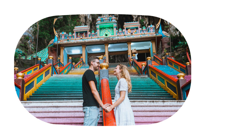 A couple looks at each other standing on the colorful stairs of Batu Caves, Malaysia